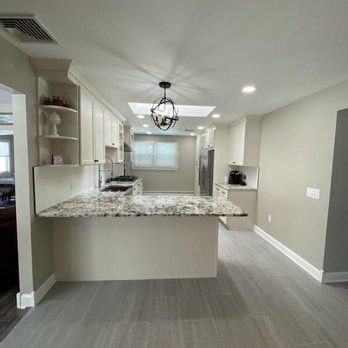 A kitchen with white cabinets , granite counter tops , and a large island.