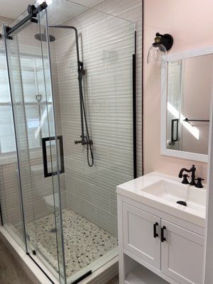 A bathroom with a walk in shower , sink and mirror.