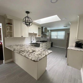 A kitchen with white cabinets , granite counter tops , a sink , and a skylight.