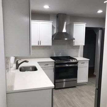 A kitchen with white cabinets , a stove , a sink , and a refrigerator.