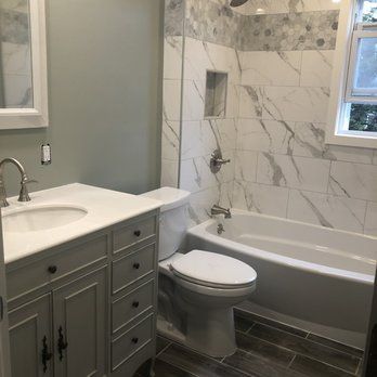A bathroom with a toilet , sink , tub and mirror.