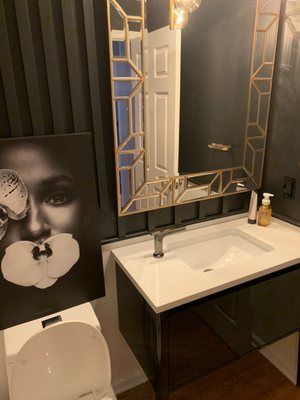 A bathroom with a sink , toilet , mirror and painting on the wall.