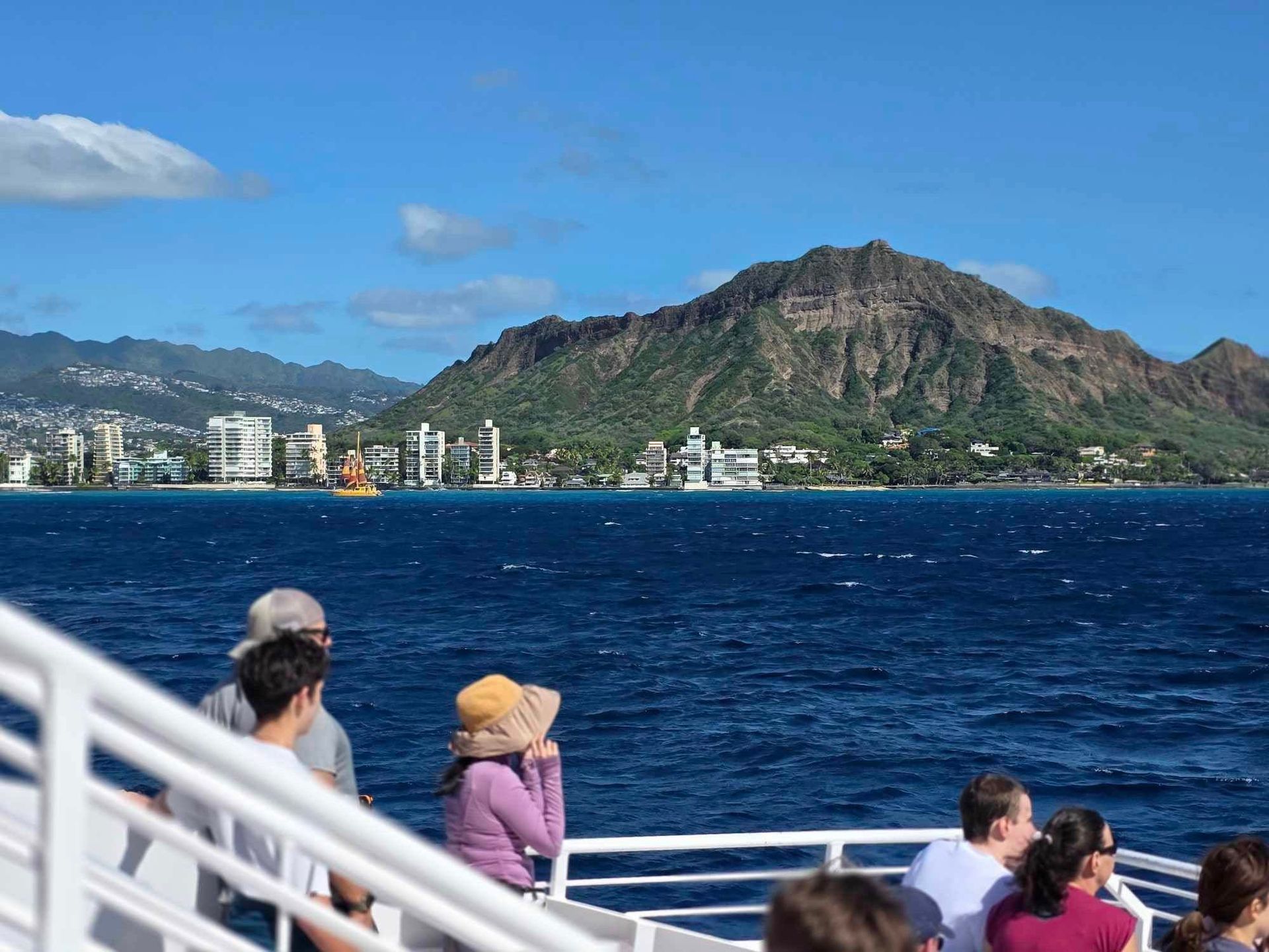 Tourists on a ferry viewing a blue ocean and rocky mountain under a clear sky