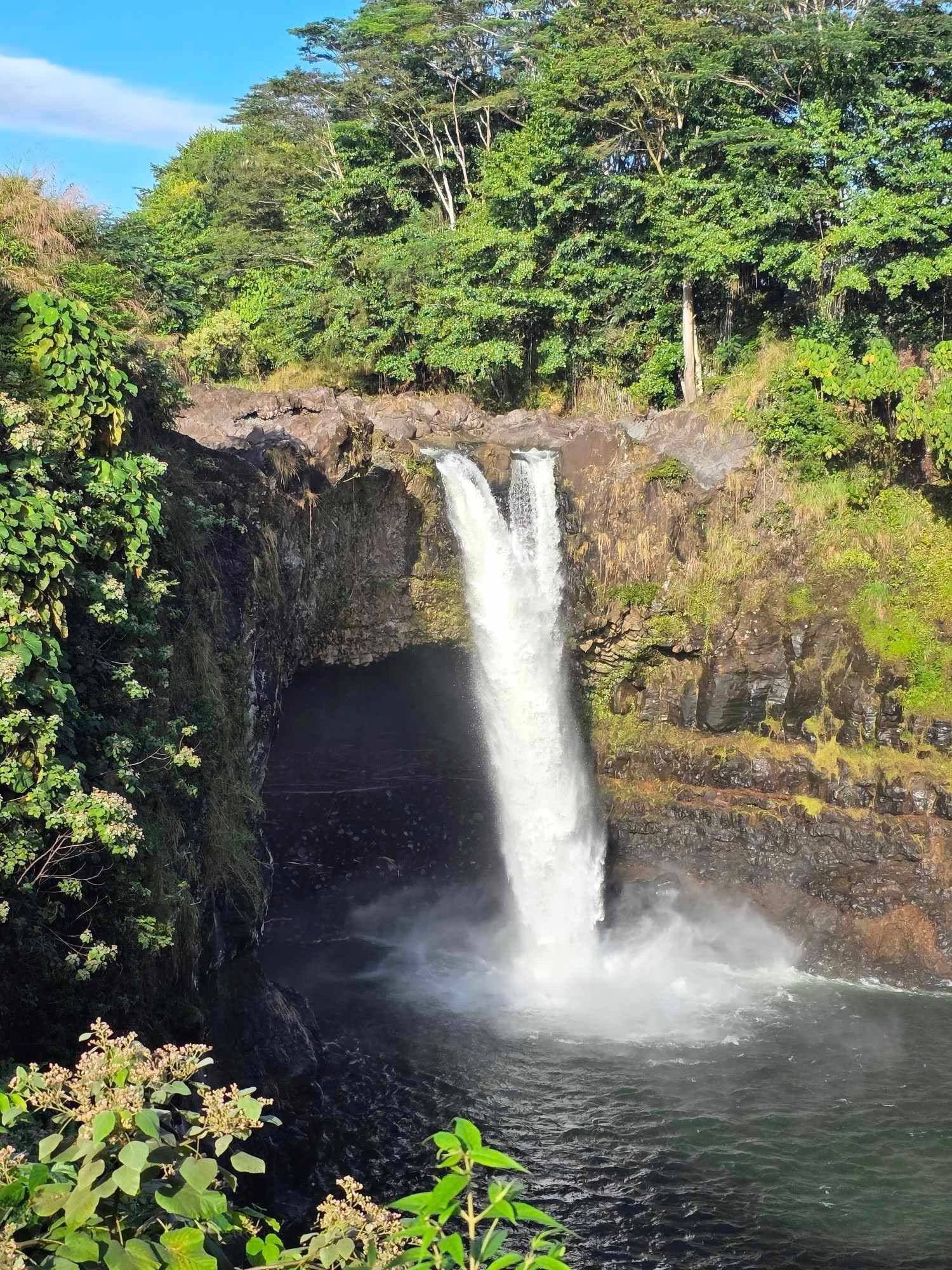 Waterfall plunging into a dark pool surrounded by lush green trees and rocky cliffs.