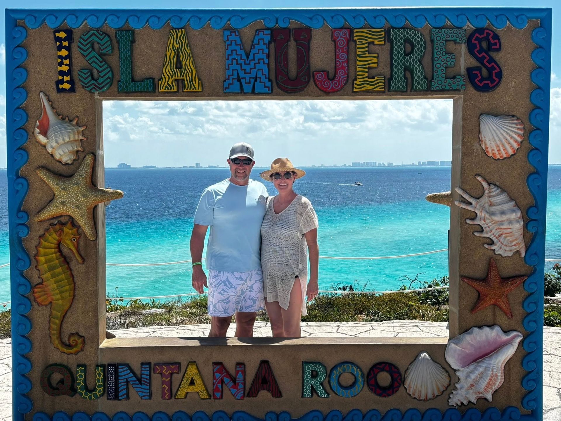 Couple posing in front of turquoise ocean within a colorful Isla Mujeres and Quintana Roo souvenir frame