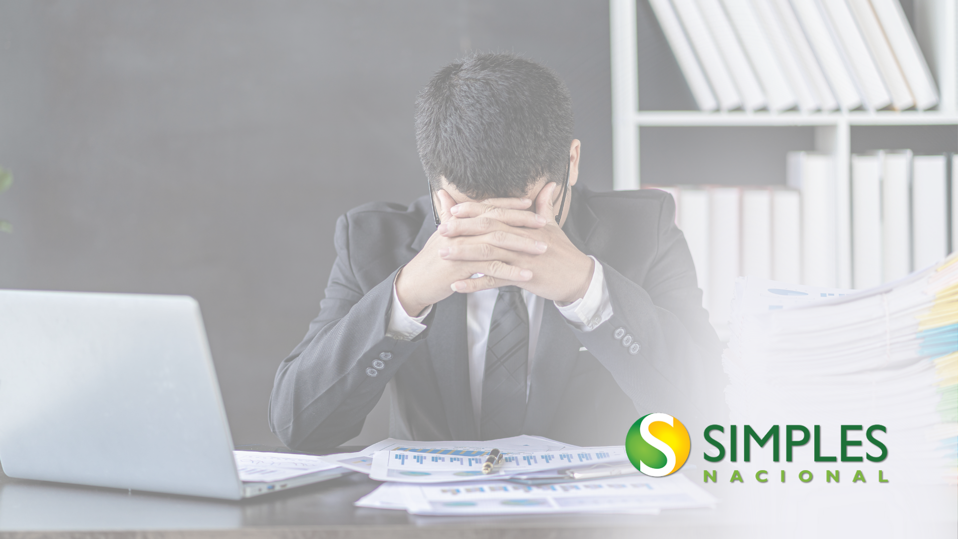 A man in a suit and tie is sitting at a desk with his head in his hands.