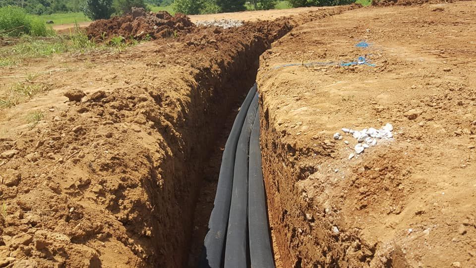 Trench dug in brown soil, with black pipes or material visible inside, outdoors.