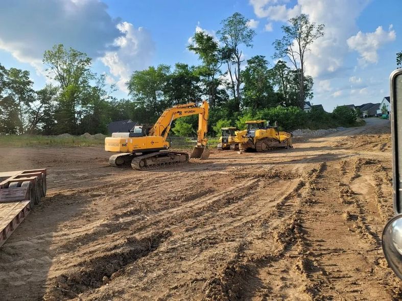 An excavator and bulldozer on a construction site, moving earth under a blue sky.