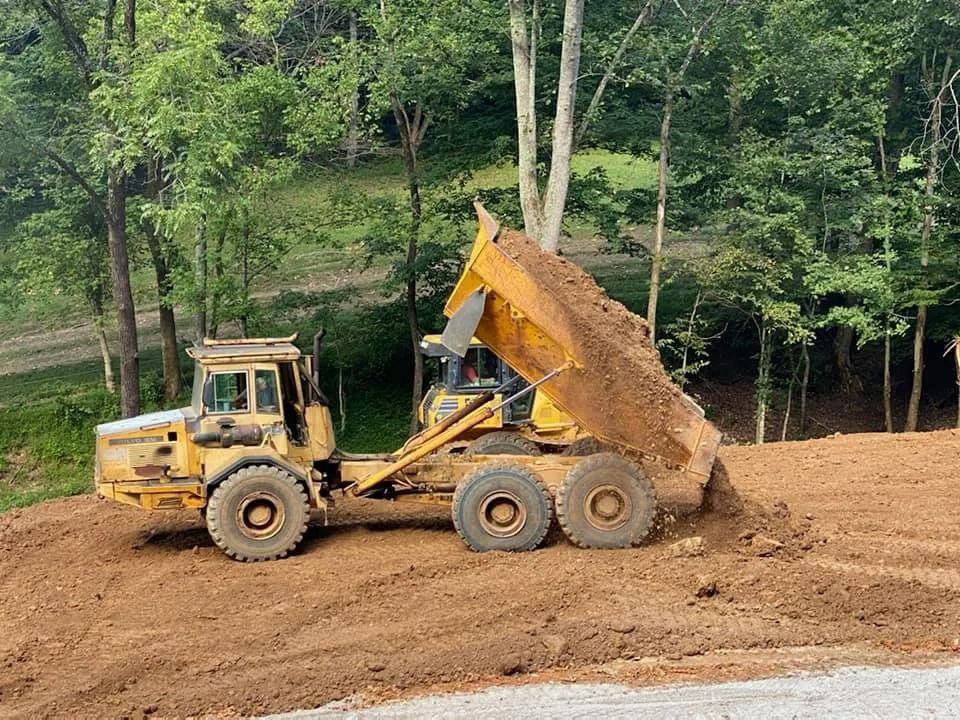 Yellow dump truck unloading dirt on a construction site with trees in the background.