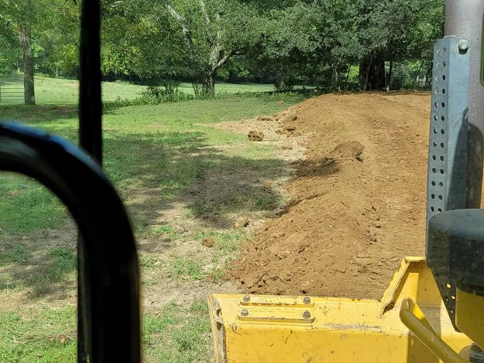 A bulldozer pushing a mound of dirt in a grassy field on a sunny day.