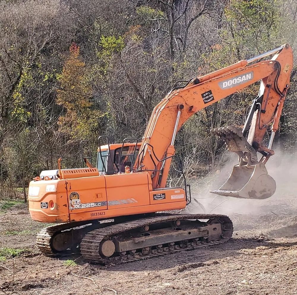Orange Doosan excavator working in a wooded area. The bucket is raised with dirt.