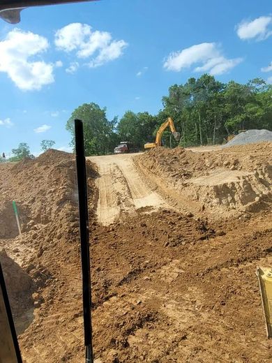 Construction site with an excavator and truck. A dirt ramp is in the center with a blue sky background.