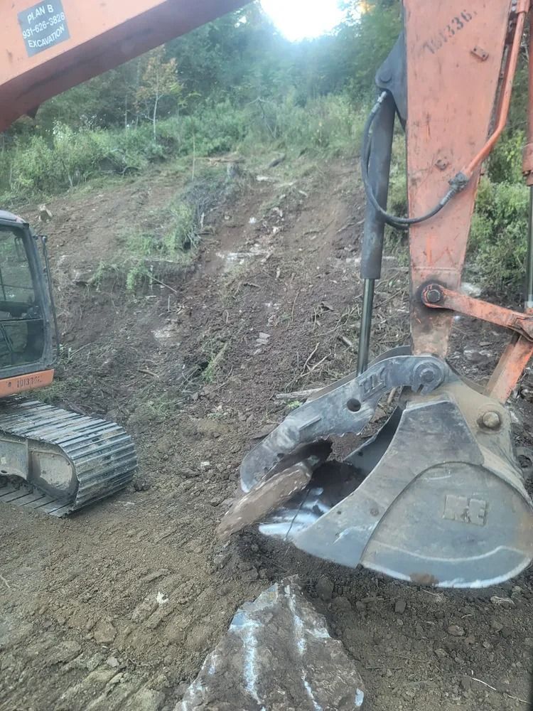 An excavator with a rock in its bucket is working on a hillside.