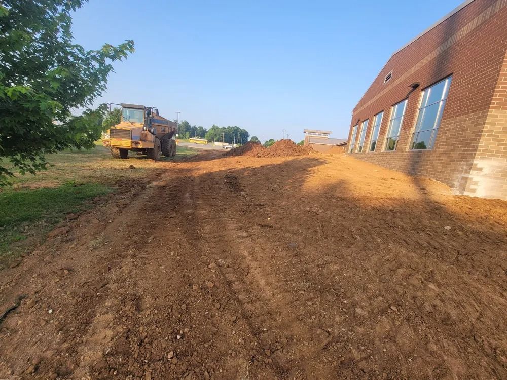 Bulldozer moving dirt next to a brick building under a clear blue sky.