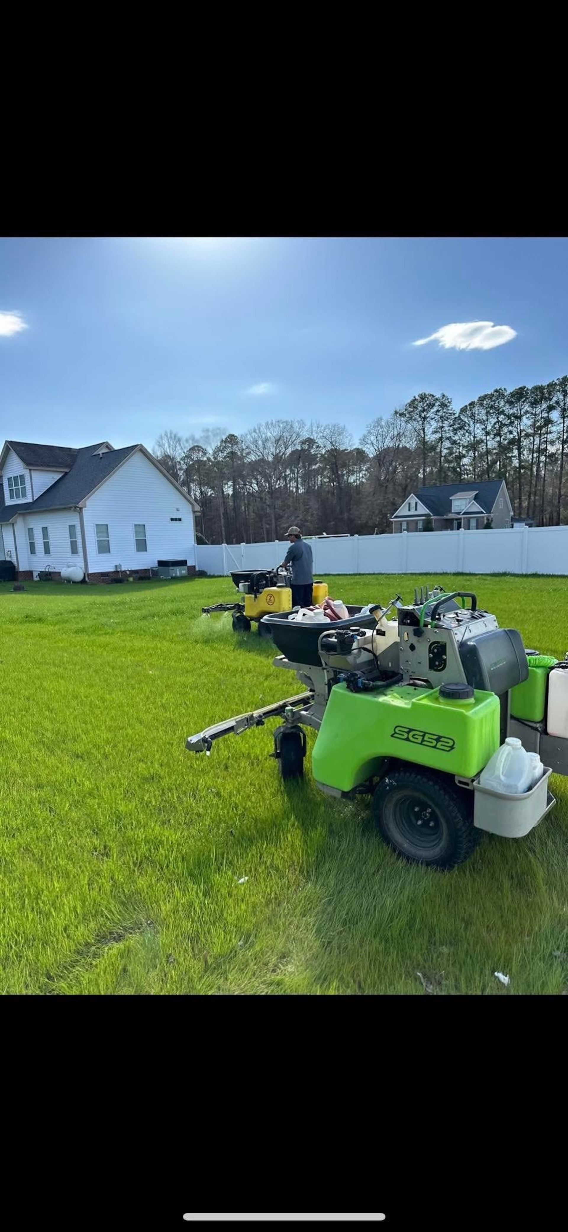 A green lawn mower is parked in a grassy field in front of a house.