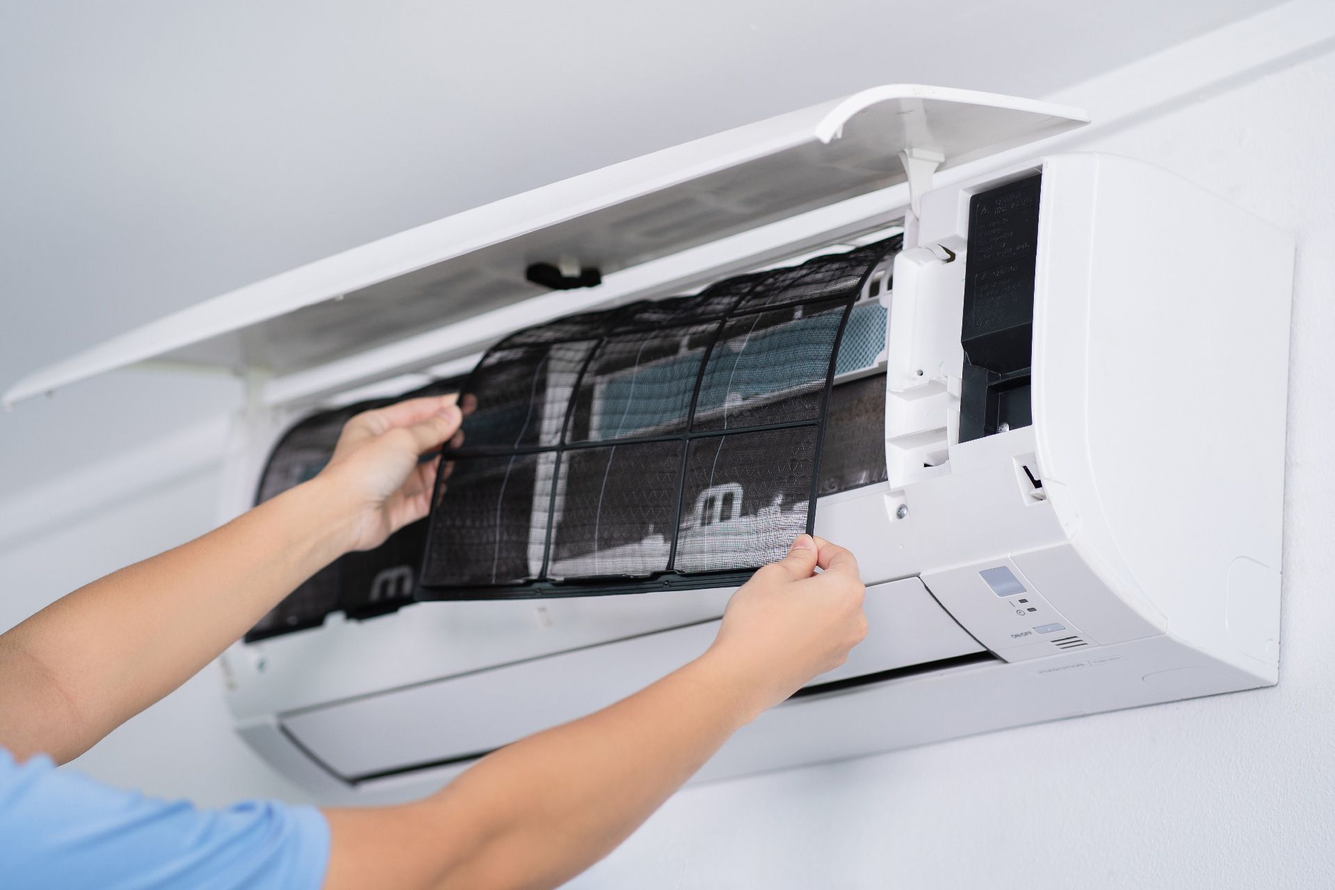 Persona limpiando el filtro de un aire acondicionado. Unidad de aire acondicionado blanca sobre una pared blanca.
