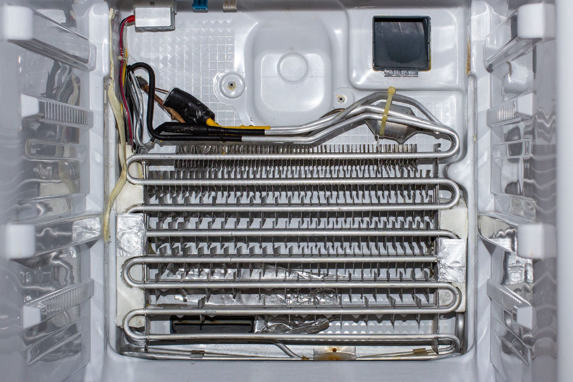 Interior de un congelador, mostrando las bobinas del evaporador, los cables y el aislamiento.