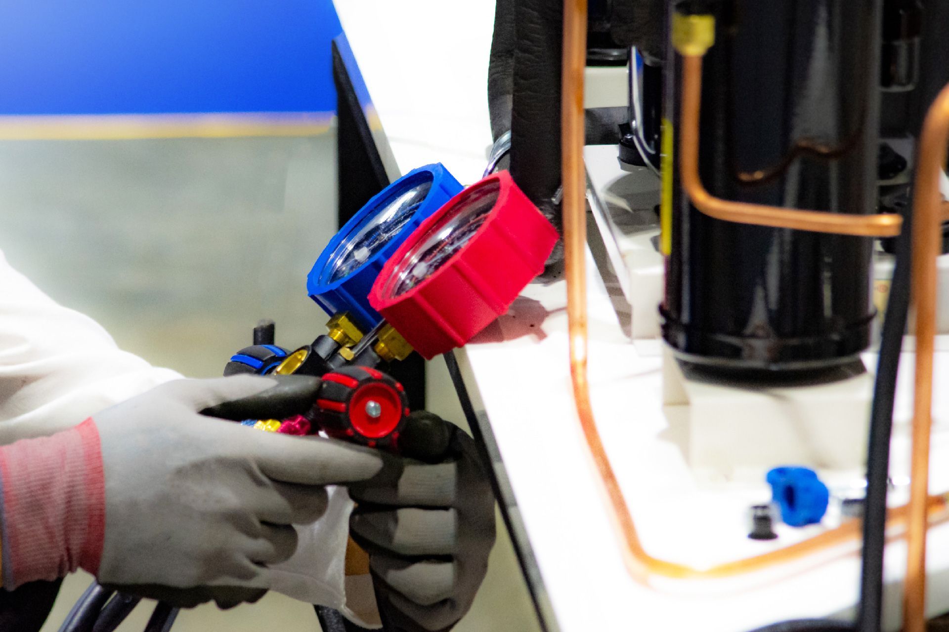 Una persona con guantes utiliza medidores para realizar el mantenimiento del aire acondicionado y conecta mangueras; medidores rojos y azules visibles.