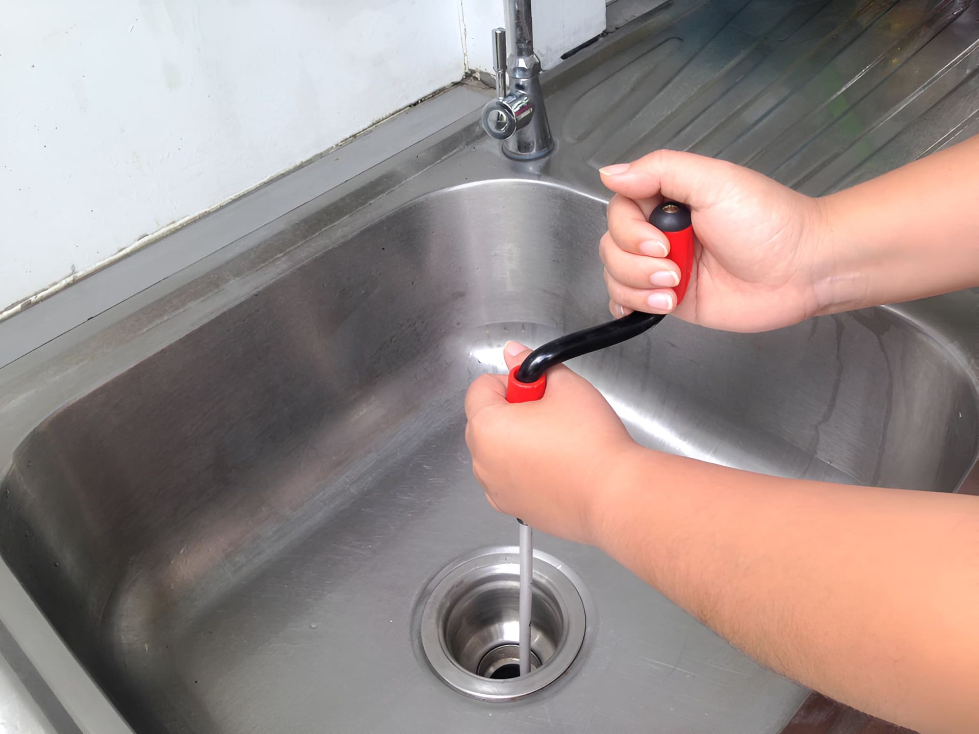 A Person is Using a Snake to Unblock a Sink Drain — John Day Plumbing in Berrimah, NT