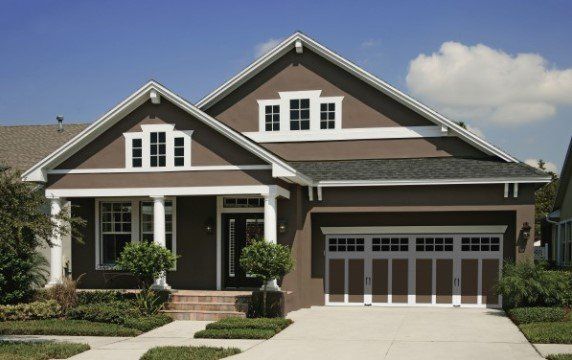 A brown suburban house with white trim, a gabled roof, a covered porch, and an attached two-car garage.