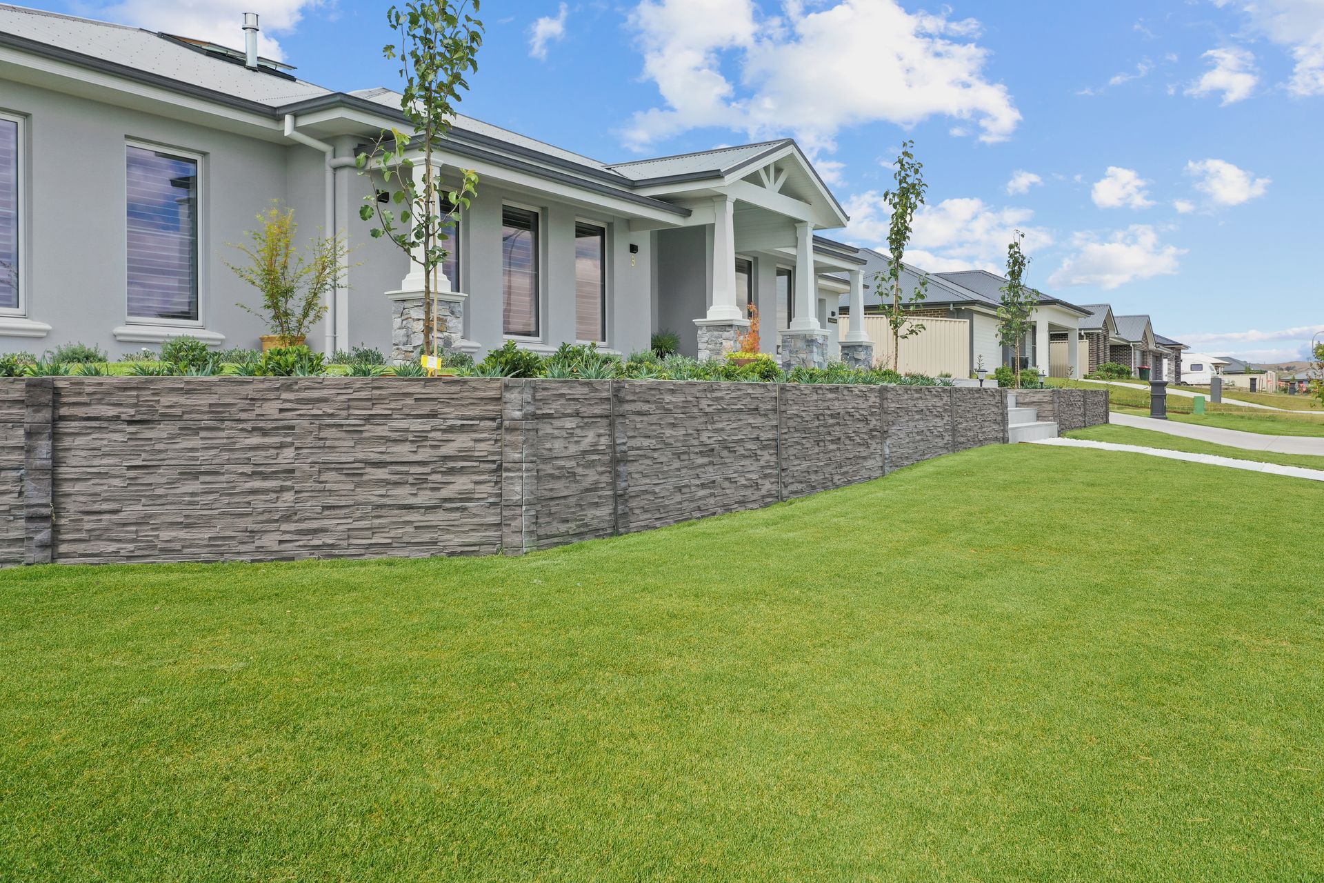 Manicured lawn, concrete sleeper retaining wall with raised native garden beds in a residential modern landscape construction