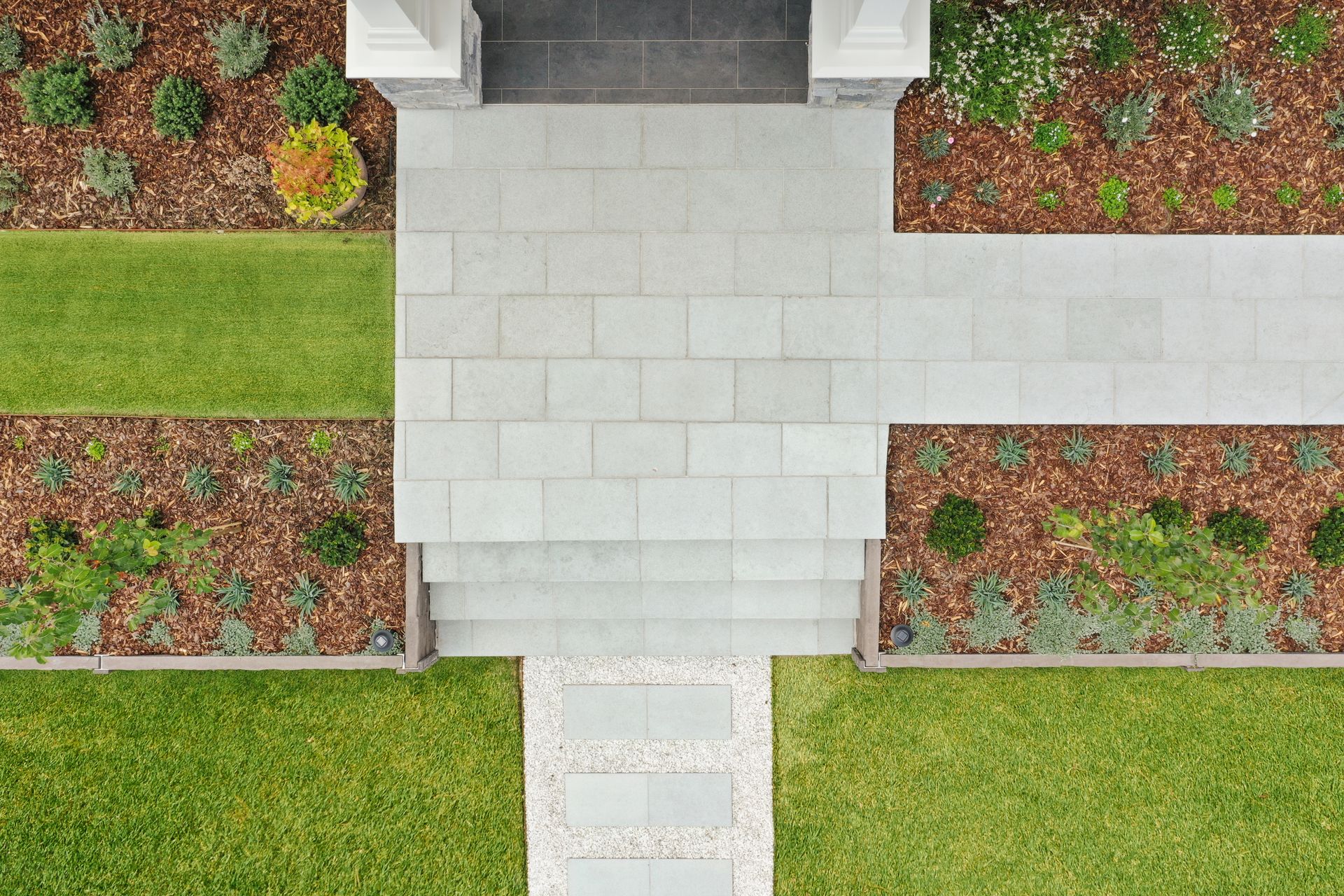 Symmetrical paved area meeting lawn and formal garden beds in modern residential landscape construction