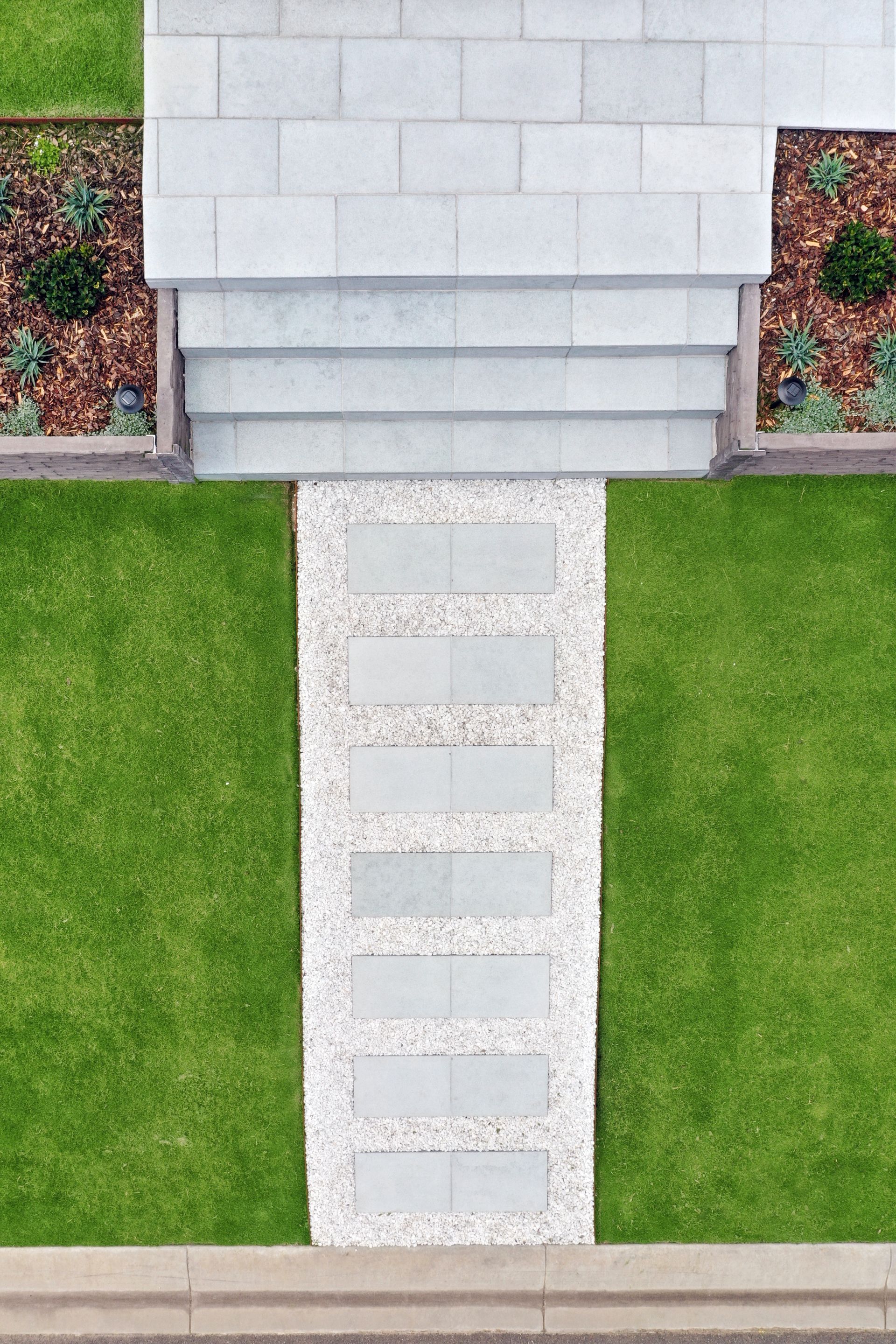 Modern residential landscape construction of a paved entrance, concrete sleeper retaining wall meeting a manicured lawn