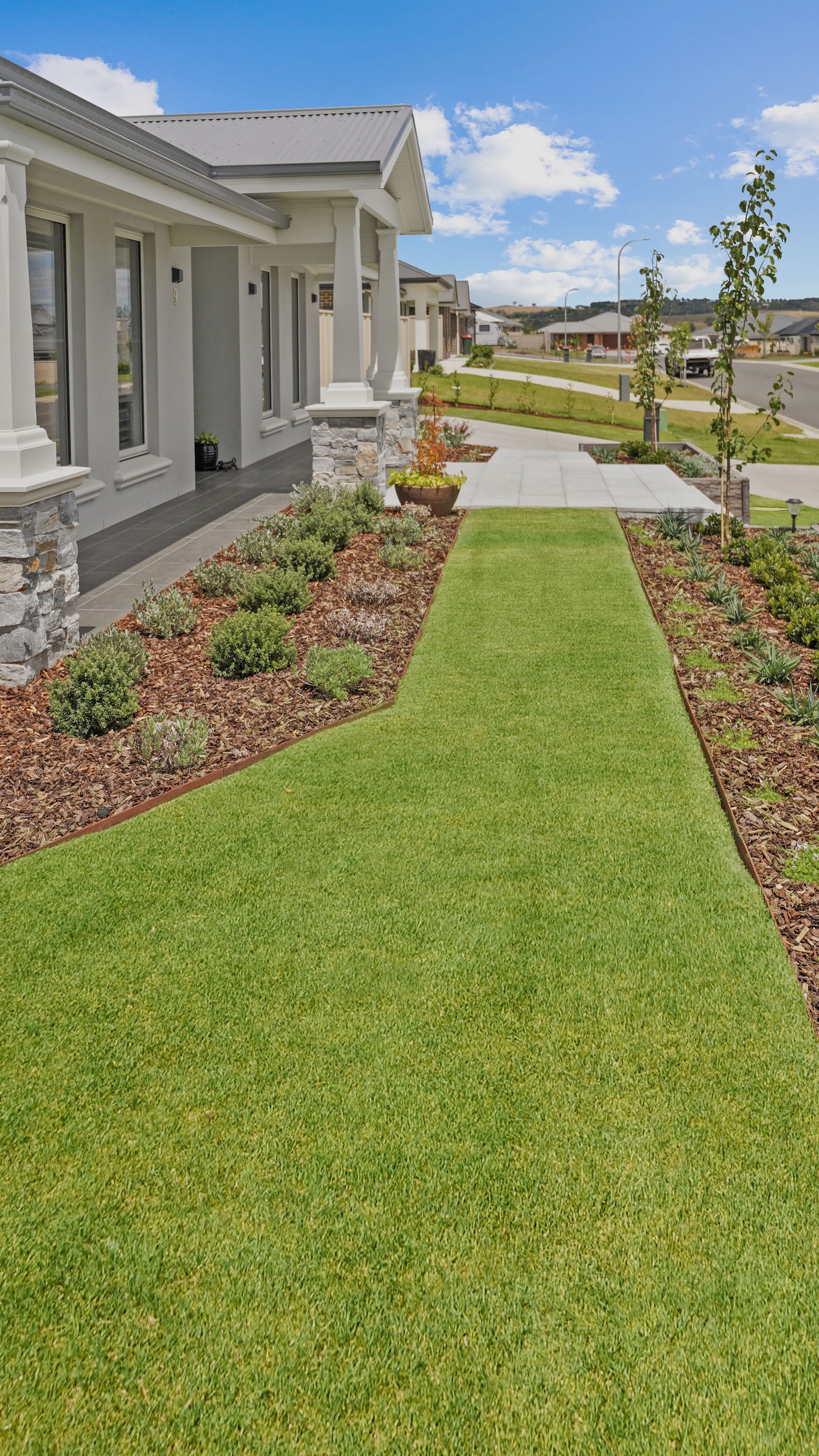 Modern landscape with native garden beds with steel edging, manicured lawn, stone cladding and paving in a residential landscape