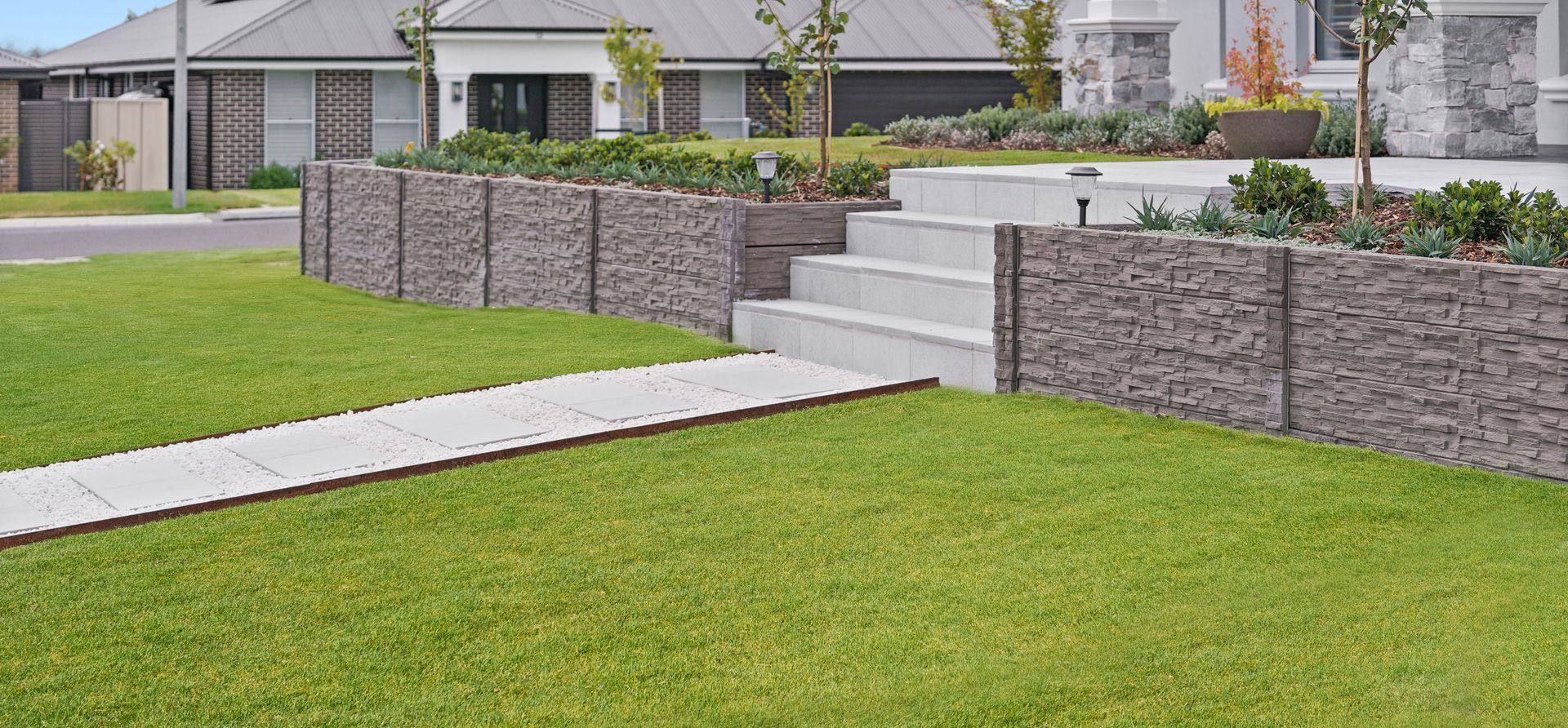 Modern residential landscape construction of a concrete sleeper retaining wall with paved areas and formal gardens