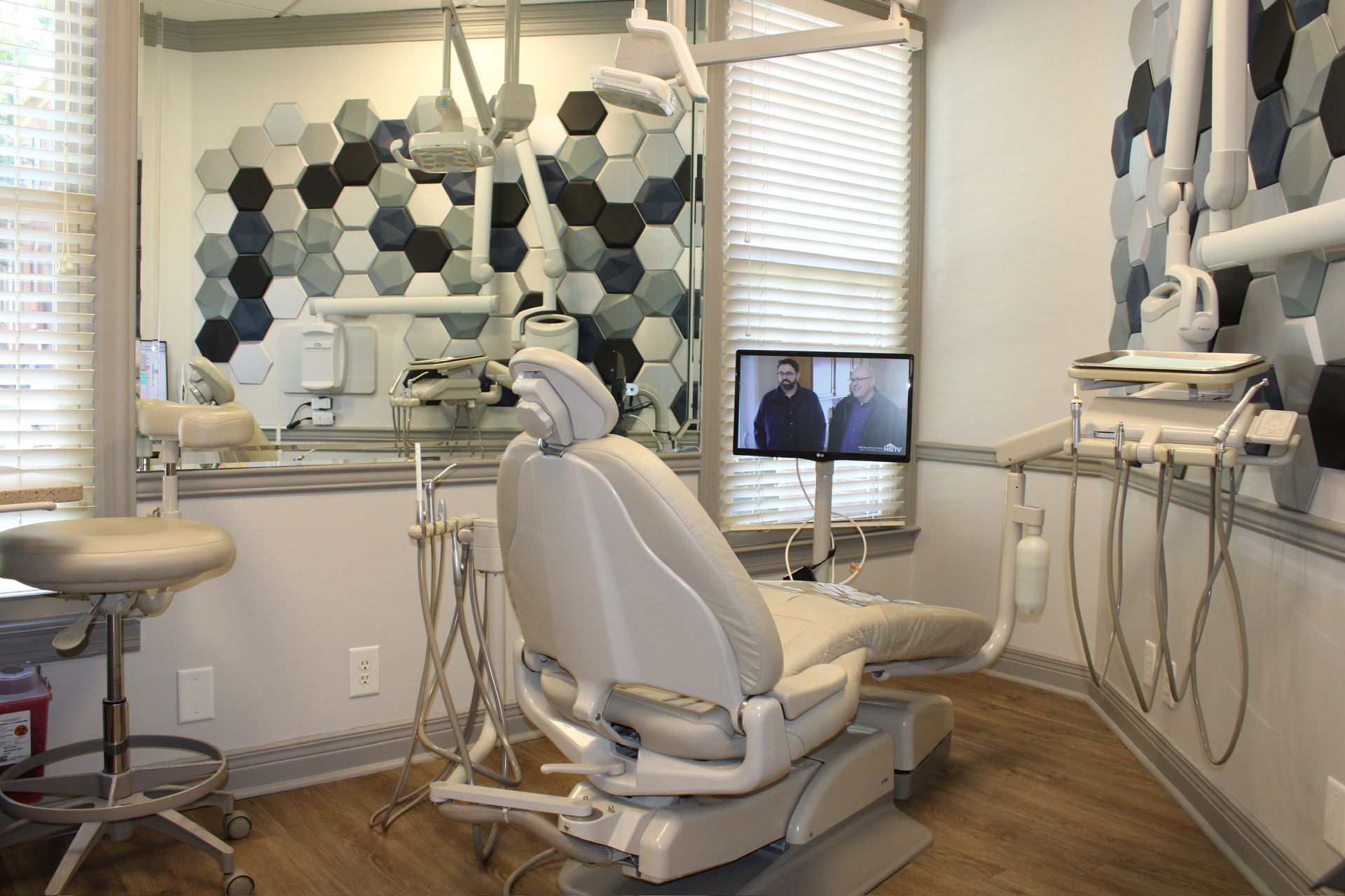 Dental exam room with chair, equipment, and hexagonal tile wall.