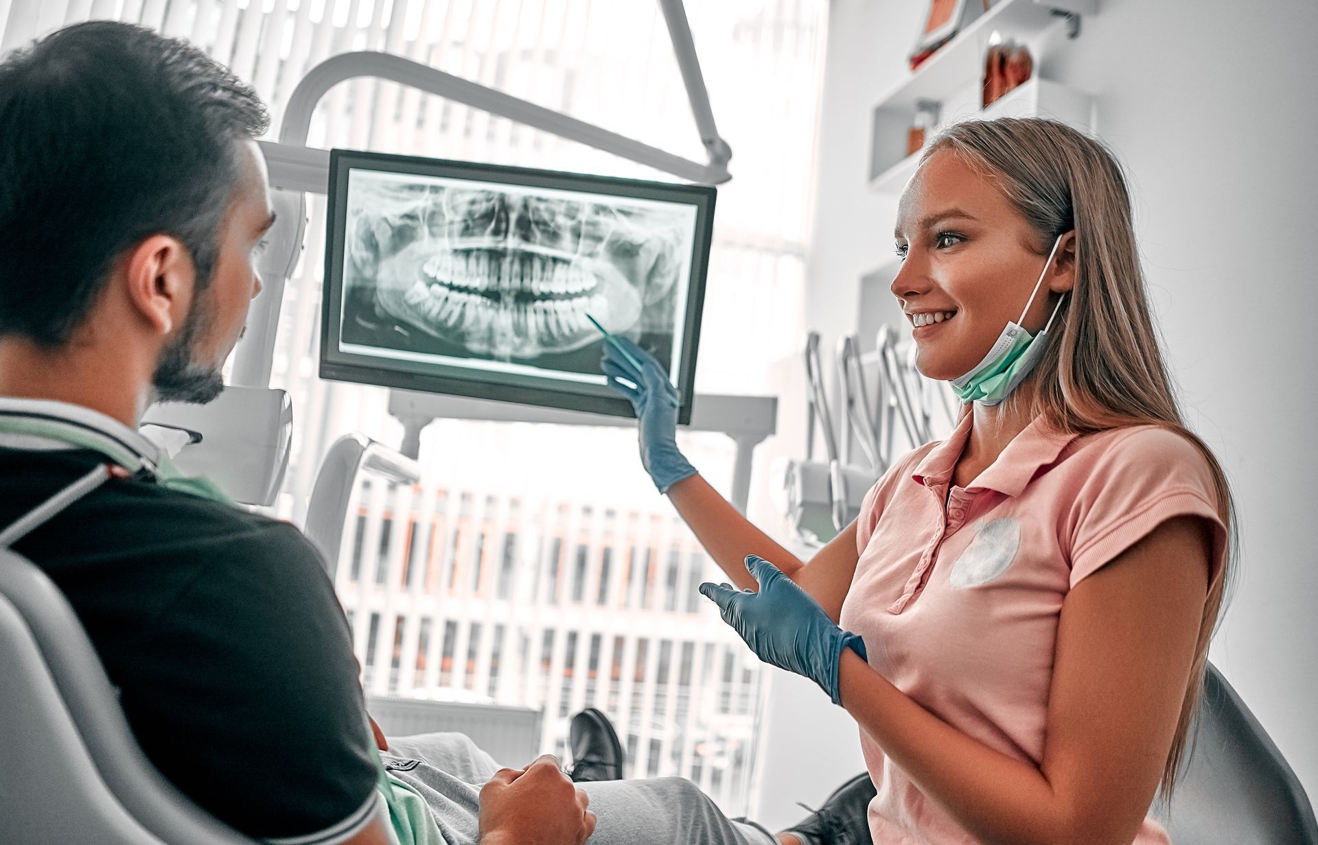 Dentist showing dental X-ray to patient, pointing. Setting is a dental office. Both are smiling.
