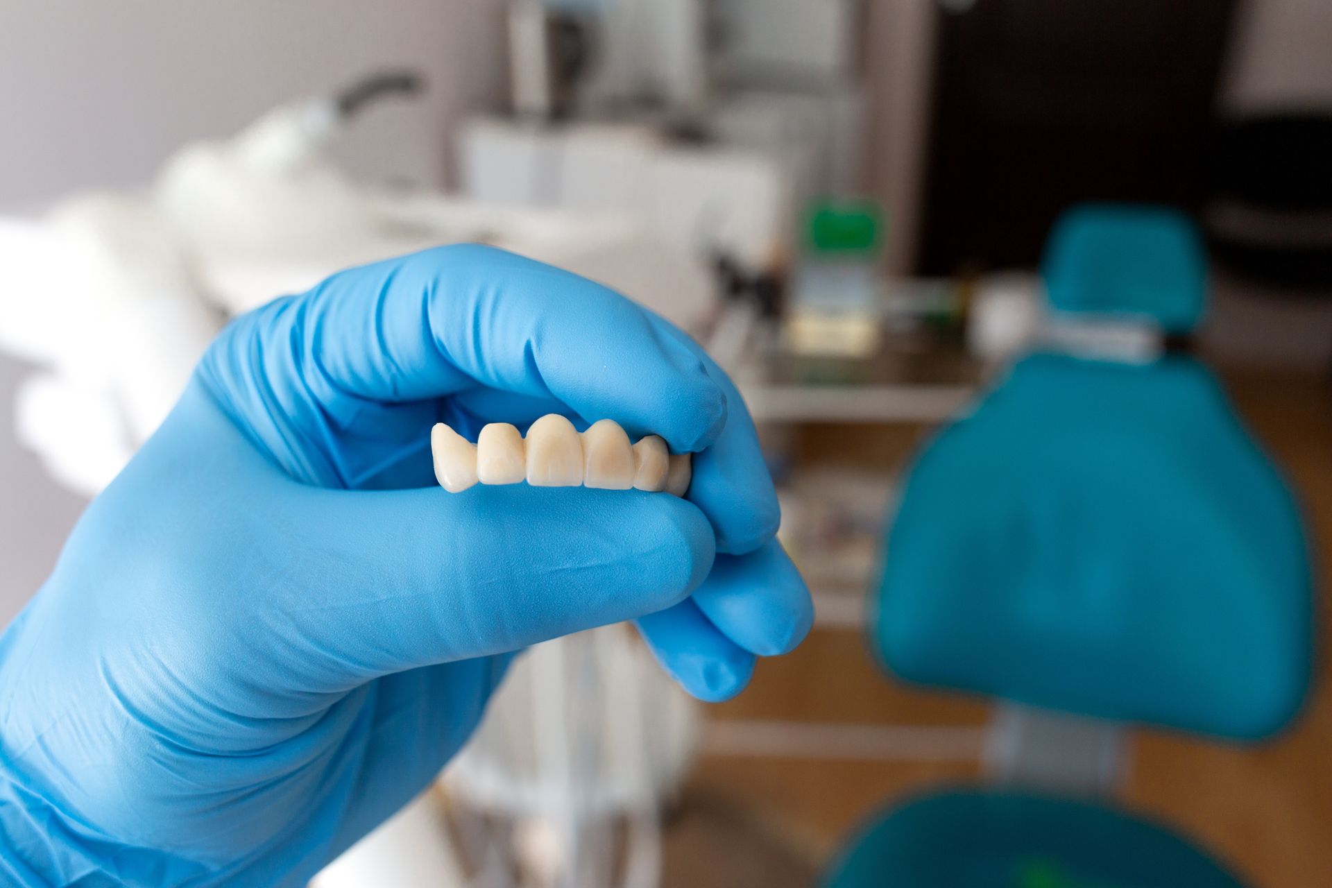 Gloved hand holding a set of false teeth in a dental office setting.