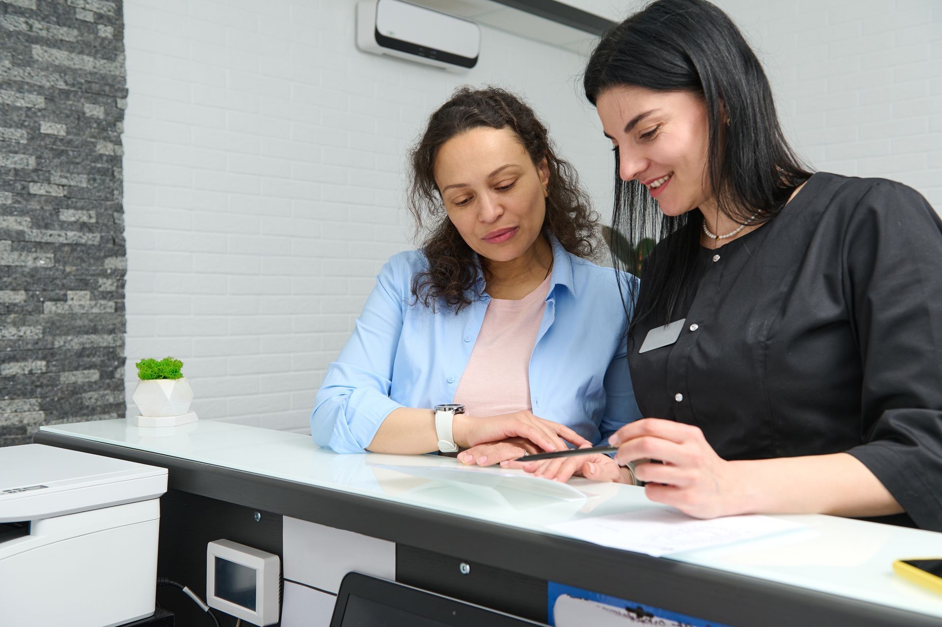Woman at reception desk with staff member reviewing paperwork.