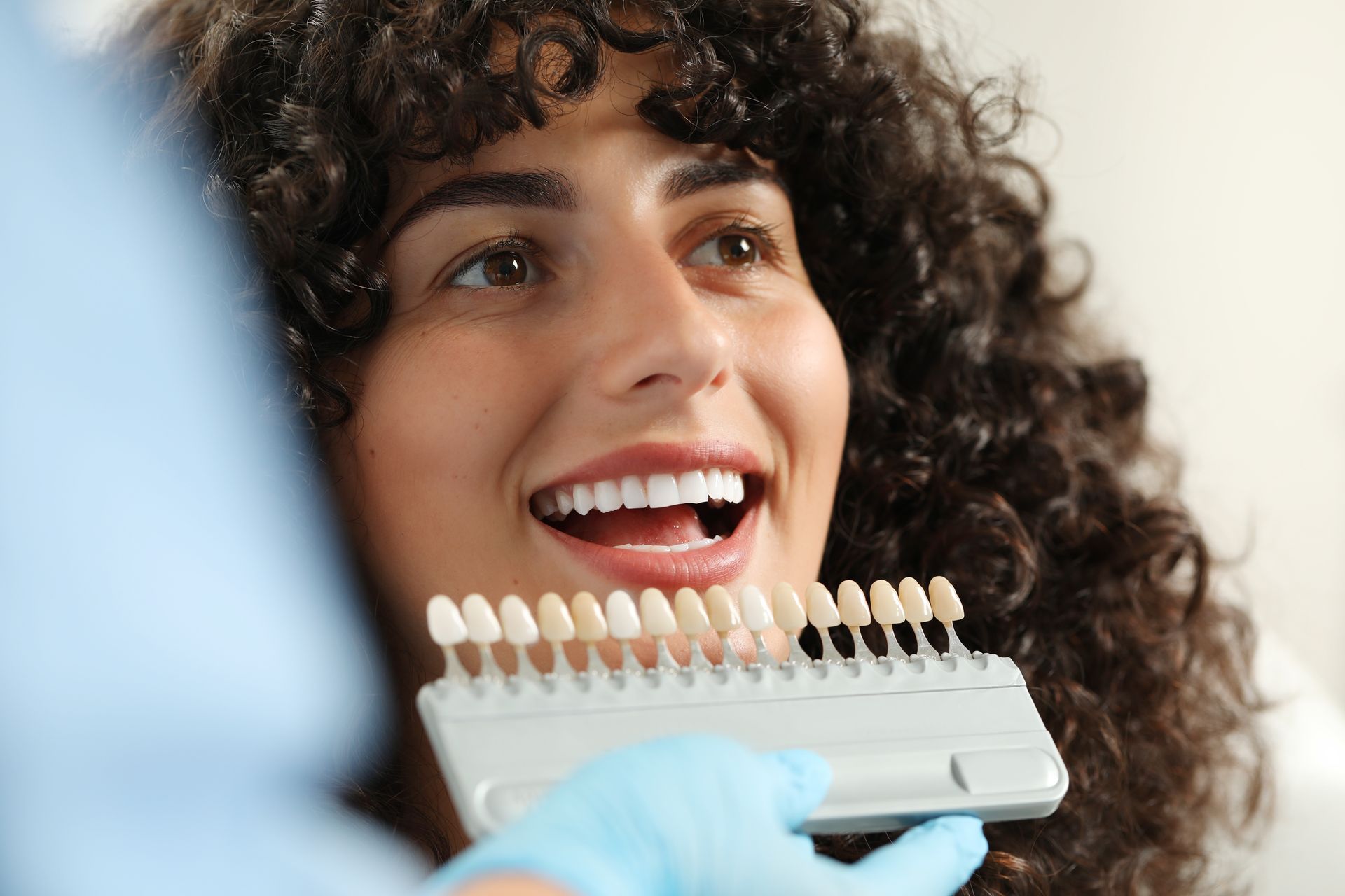 Woman smiling, comparing teeth shade with dental color guide.