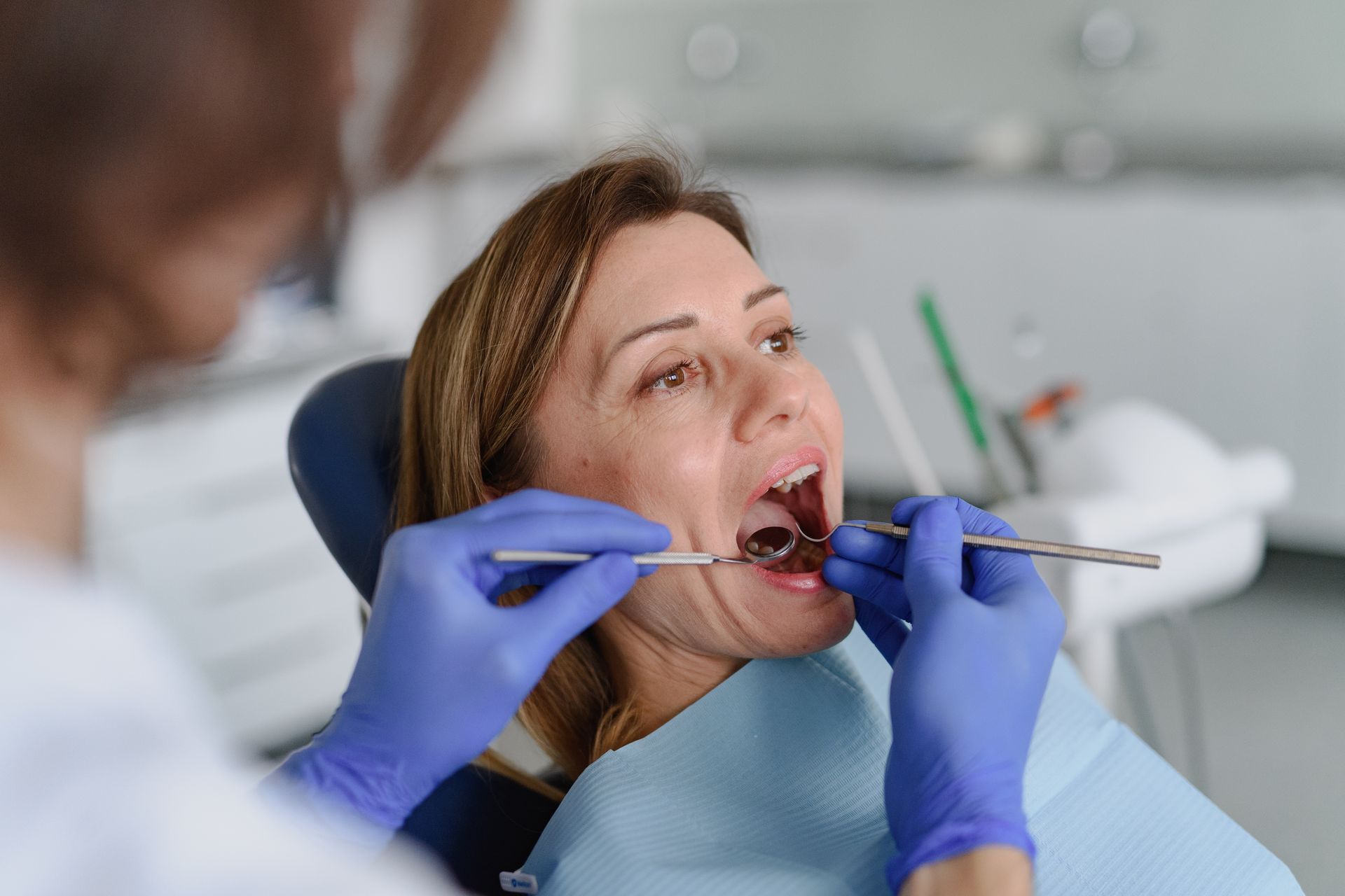 Dentist examining a patient's teeth with dental tools in a clinic setting.