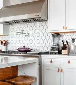 A kitchen with white cabinets , a stove , a blender , a pot , and a sink.