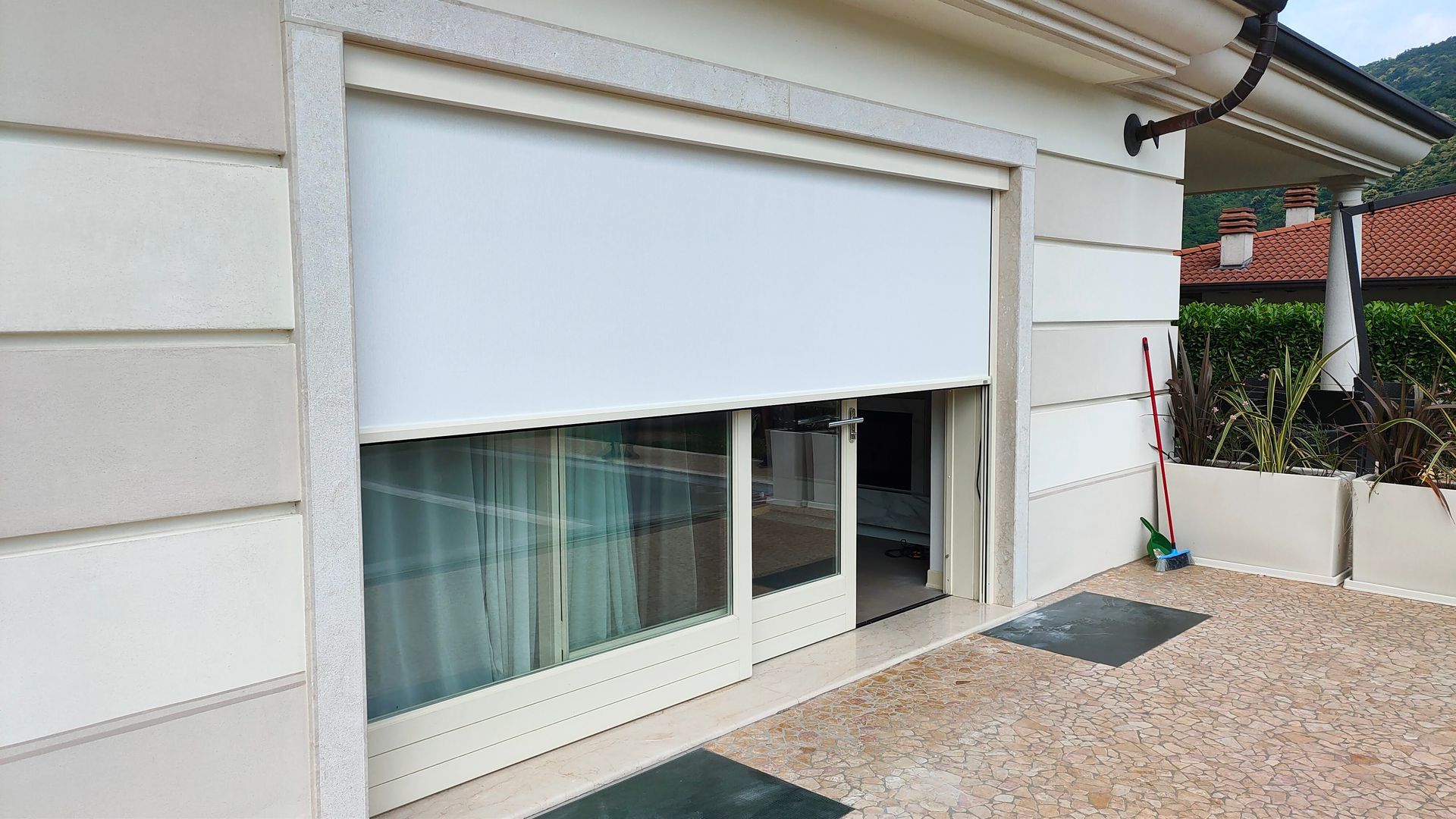 Tenda bianca parzialmente abbassata su una porta scorrevole in vetro, all'esterno.