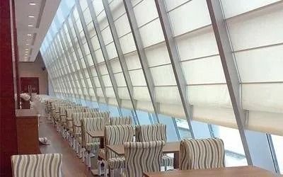 Sala da pranzo del ristorante con tavoli e sedie allineati vicino a una grande finestra coperta da tende.