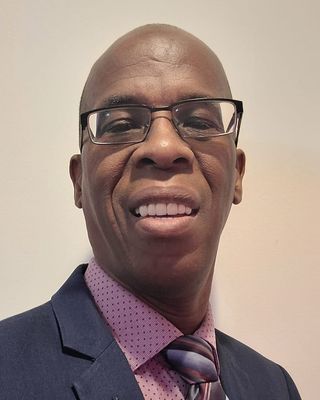Man wearing glasses, smiling, wearing a blue suit jacket, pink shirt, and patterned tie.