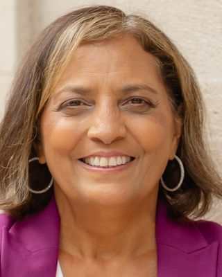Woman smiling, wearing a pink blazer and hoop earrings, outdoors.