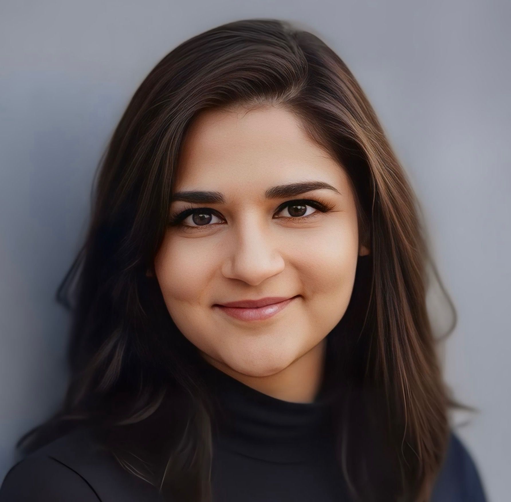 Woman with brown hair, smiling, wearing a black turtleneck, leaning against a gray wall.