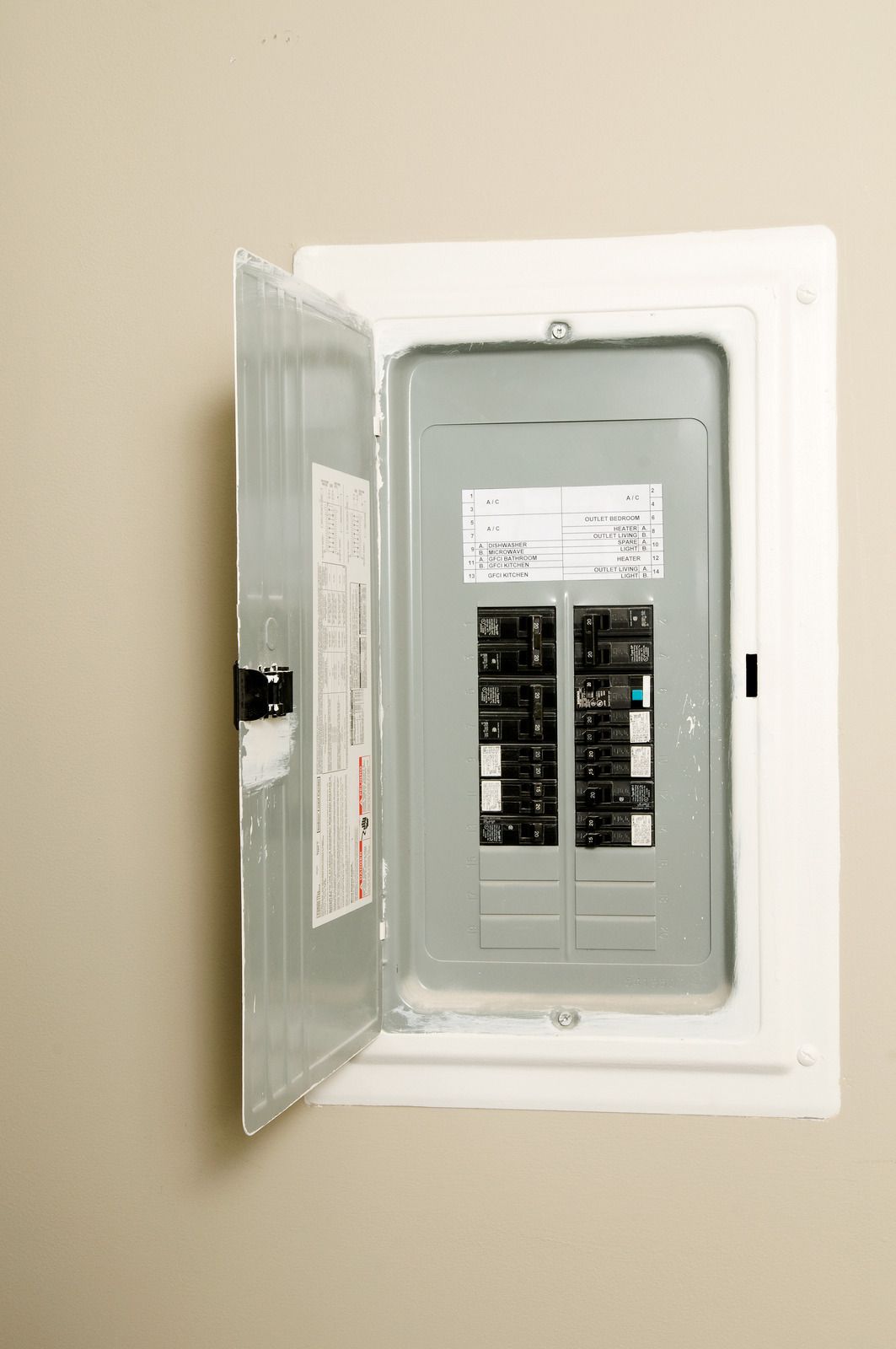 Open circuit breaker box on a beige wall; silver metal with black switches.