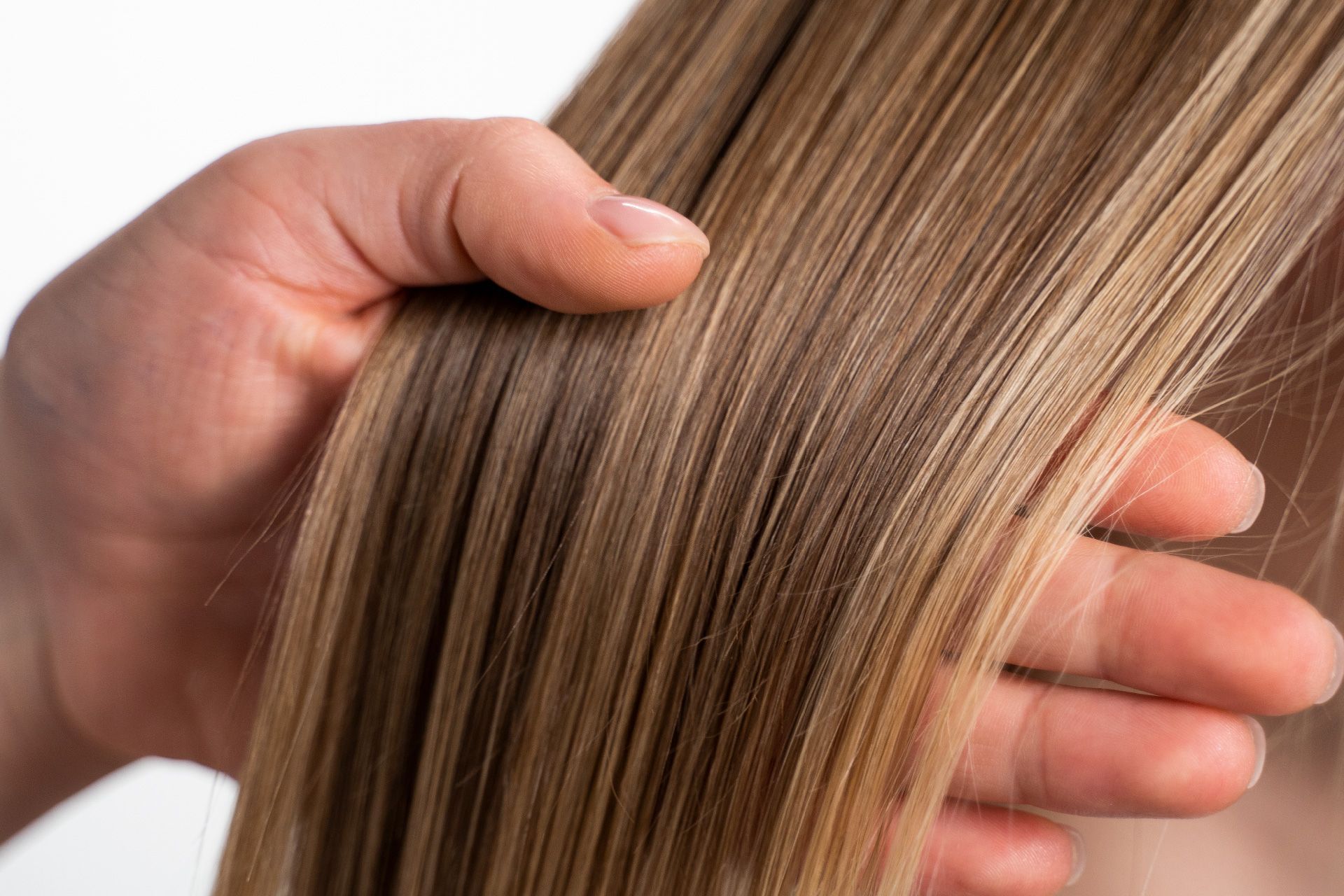 Mano pasando por un cabello liso, lacio y castaño claro con reflejos.