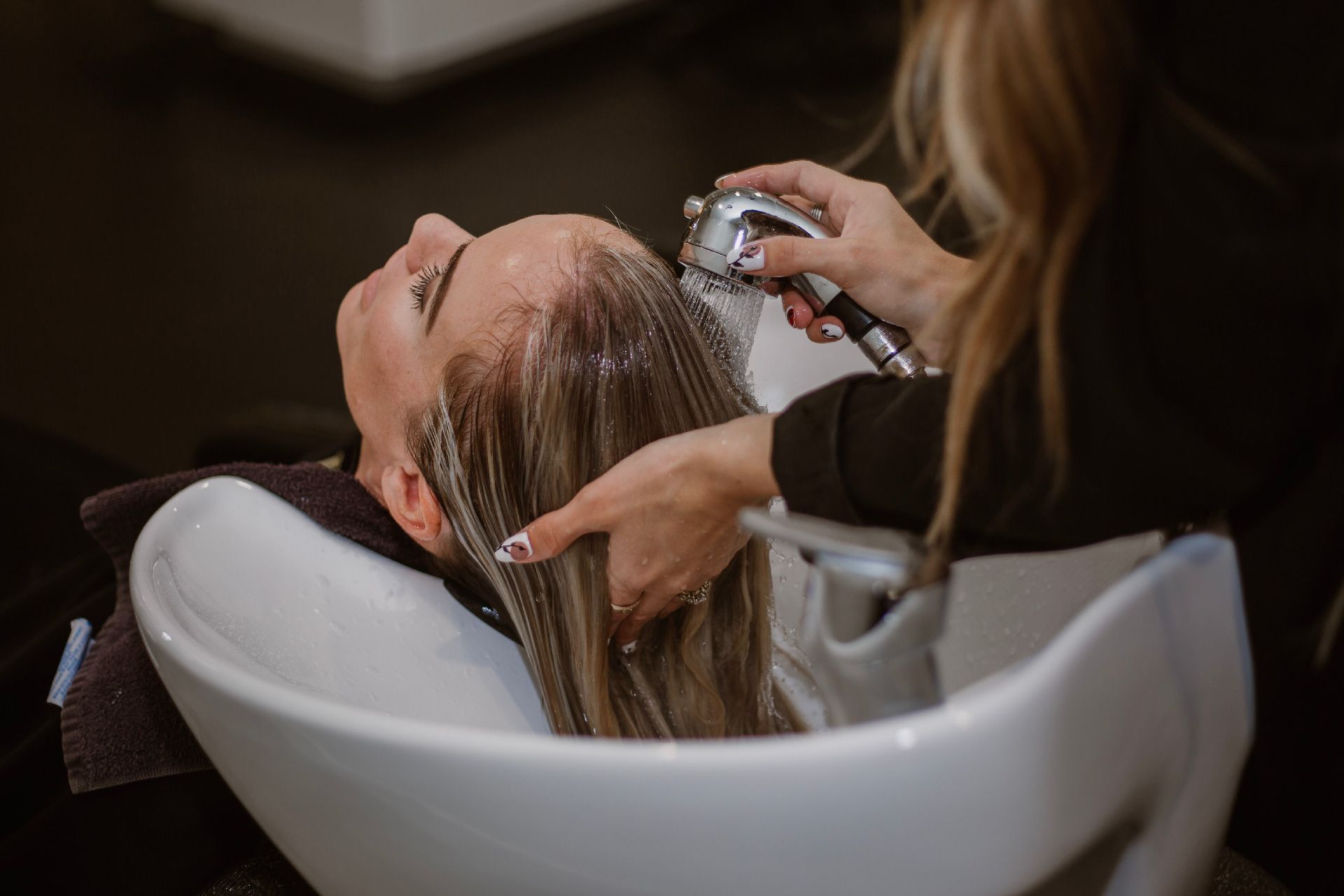 Una mujer se lava el pelo en una peluquería. El peluquero le enjuaga el champú con una ducha de mano.