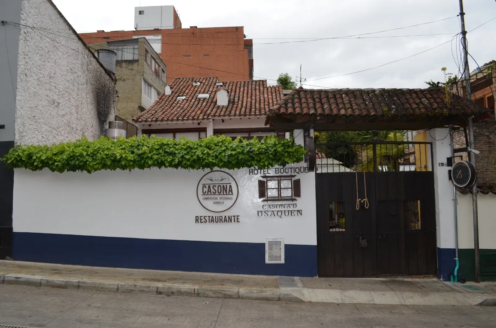 Restaurant facade with white and blue wall, a wooden gate, and a tiled roof.