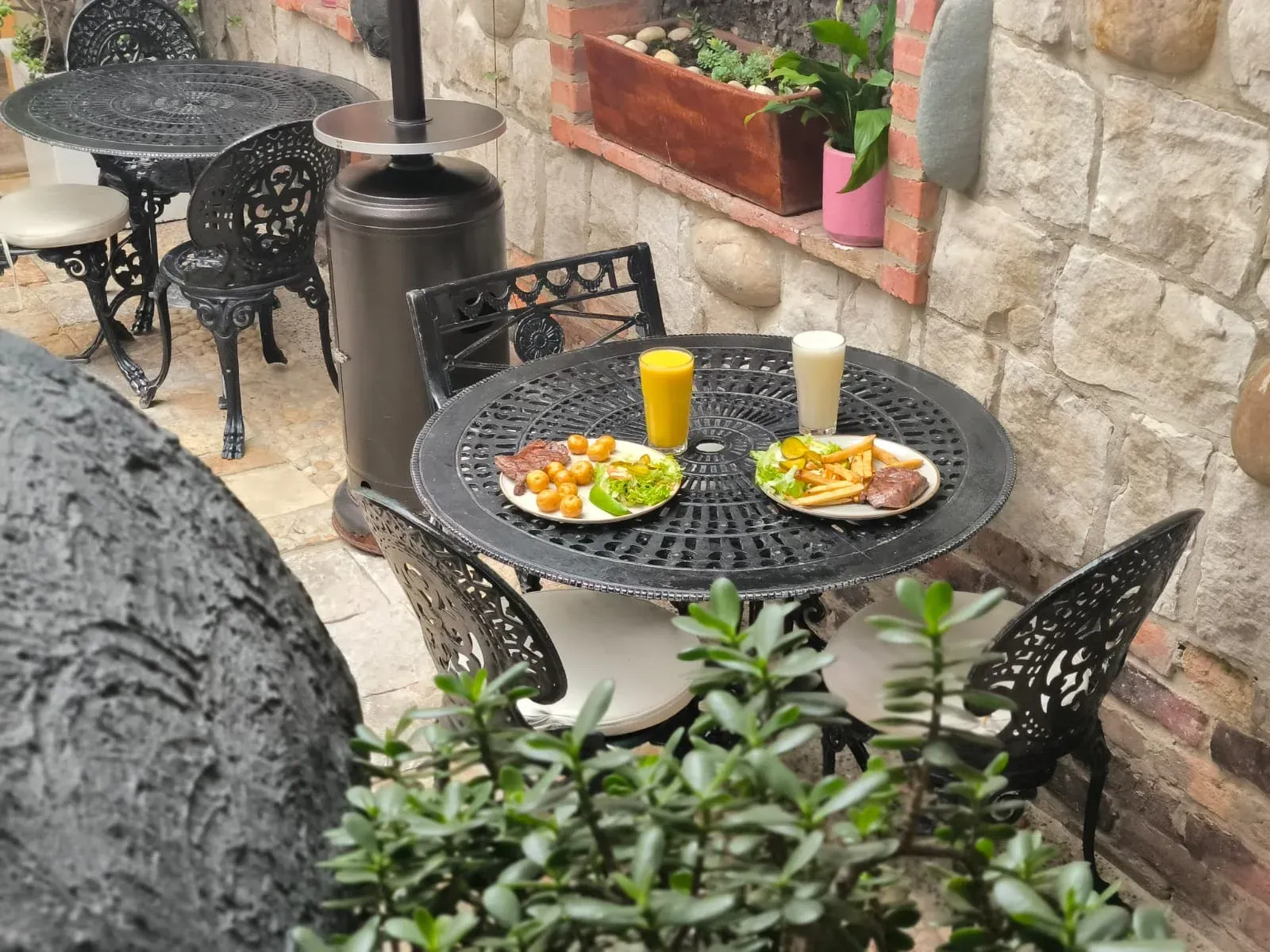 Mesa de cafetería al aire libre con comida, bebidas y muebles de hierro fundido. Fondo de pared de ladrillo.