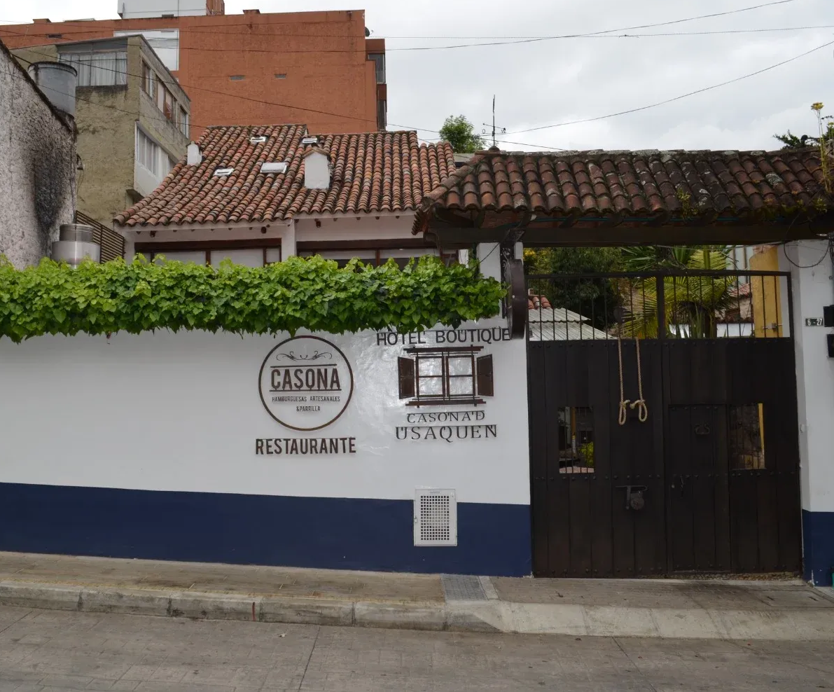 Fachada del restaurante con pared blanca y azul, puerta de madera y toldo cubierto de enredaderas.
