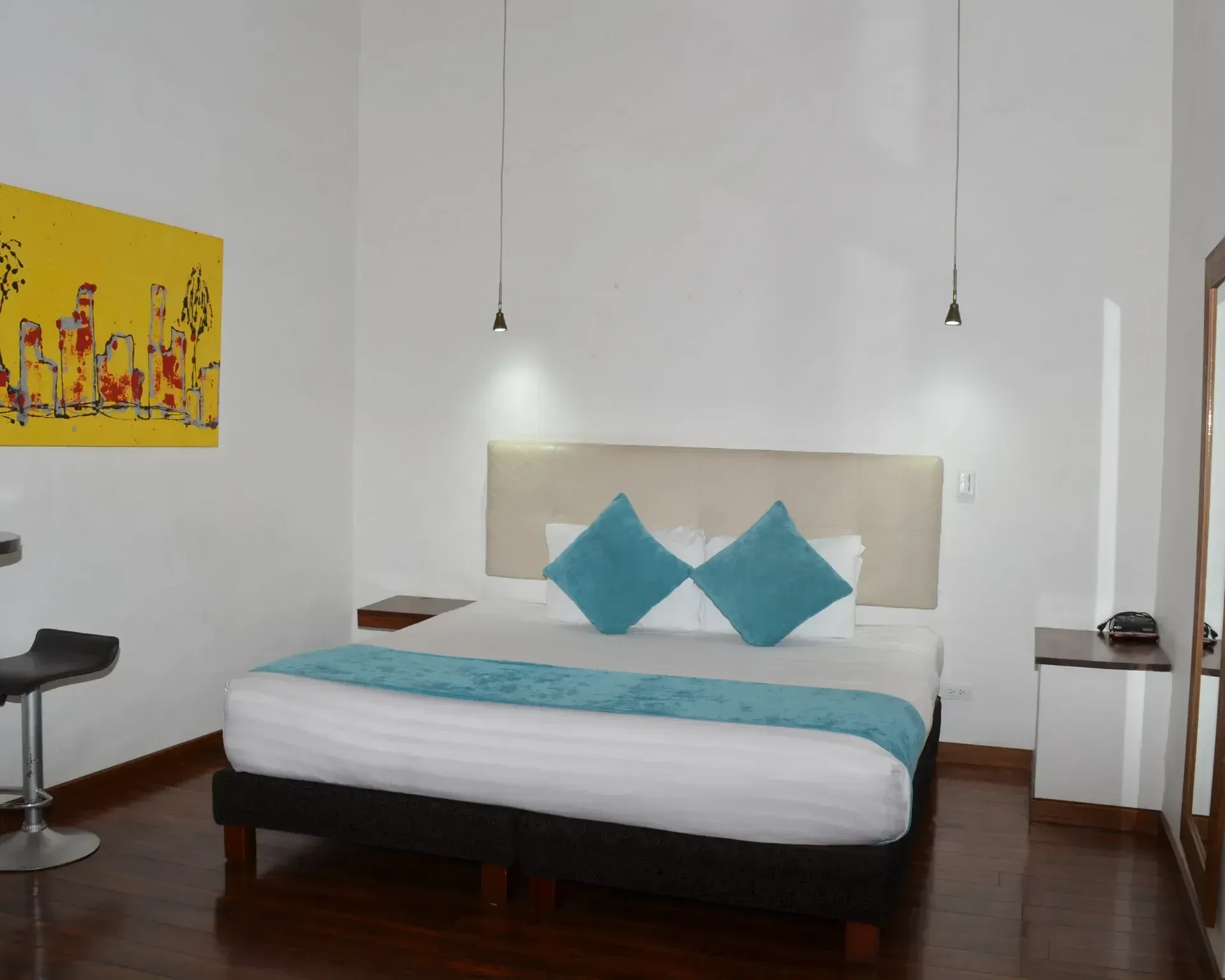 Habitación de hotel con cama, almohadas color verde azulado y un cuadro decorativo.