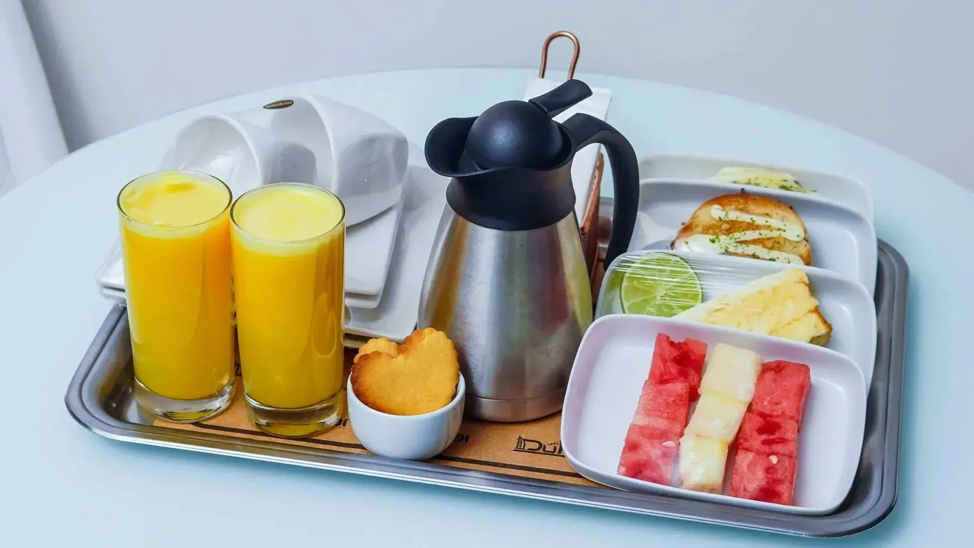 Bandeja de desayuno con dos zumos de naranja, cafetera, tostadas y fruta.
