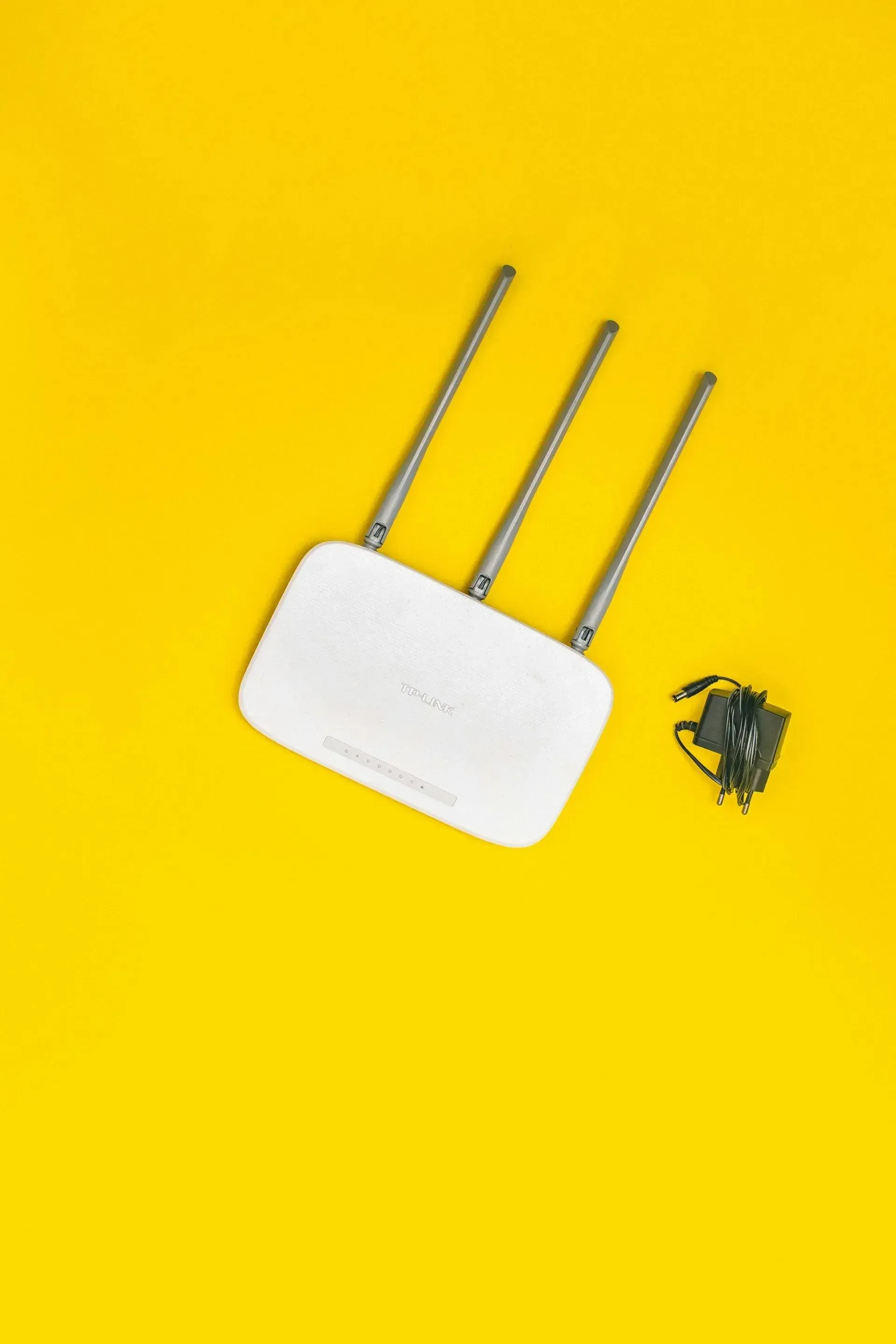 Router Wi-Fi blanco con tres antenas y adaptador de corriente sobre fondo amarillo.